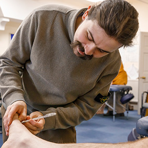 male acupuncture student holding patient’s foot