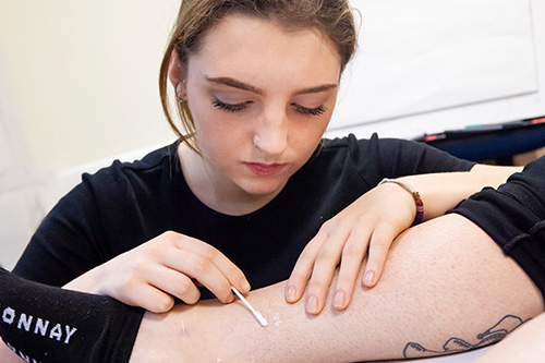 female acupuncture student using cotton swab on a patient's leg