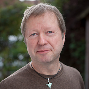 smiling man with necklace and brown jumper